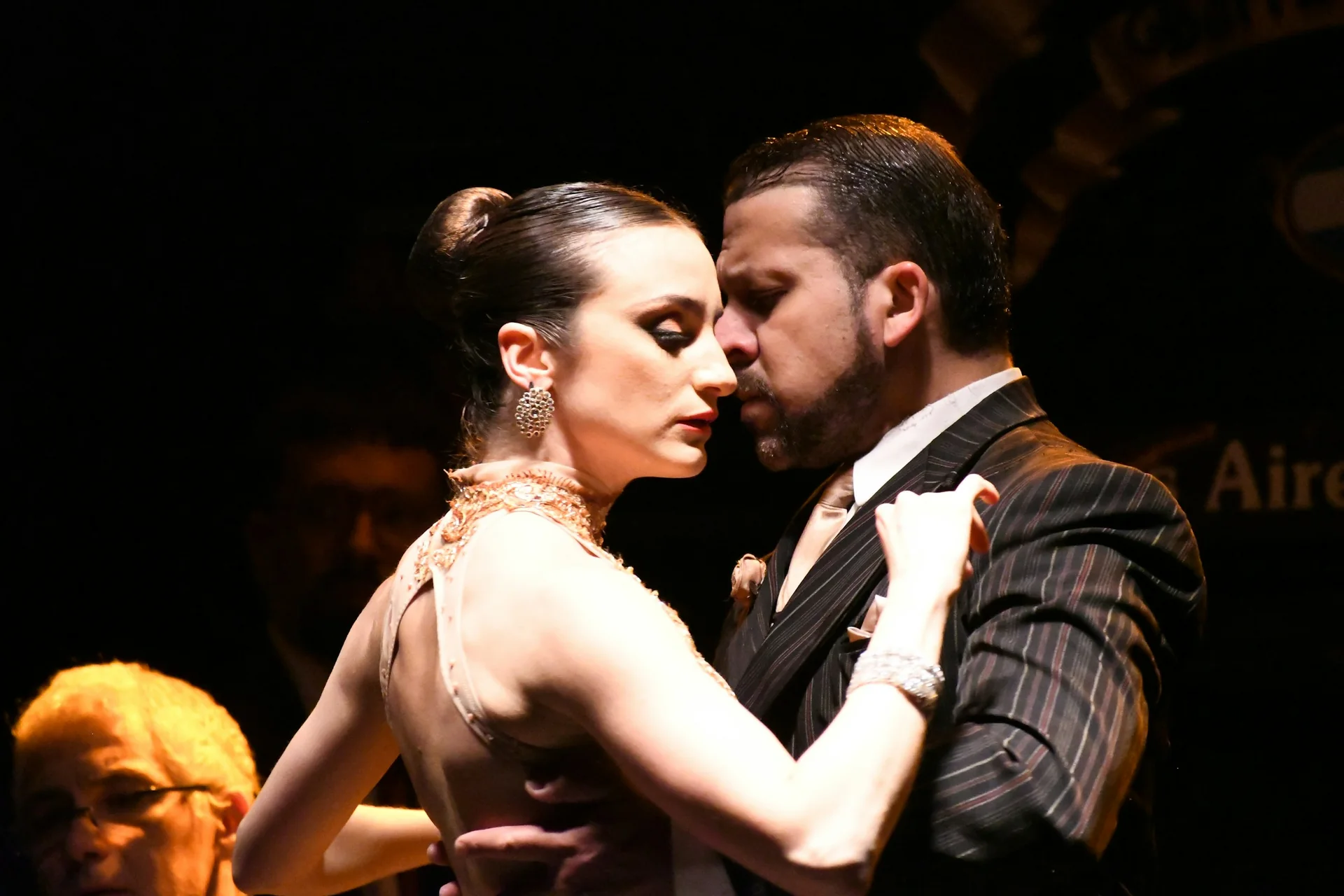 A tango couple dancing in close embrace under warm stage light, Buenos Aires