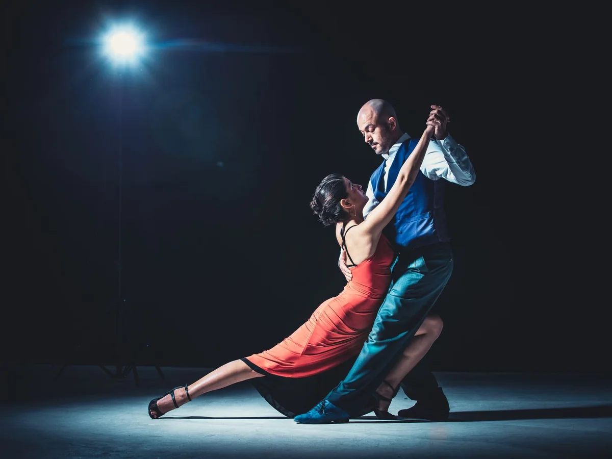 A tango couple in a deep dip under a single spotlight against a dark background (representative photograph)